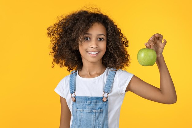 Linda chica africana sosteniendo manzana verde aislado sobre fondo amarillo