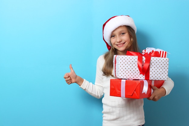 Linda chica alegre con un sombrero de navidad sobre un fondo de color sosteniendo un regalo