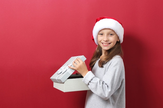 Linda chica alegre con un sombrero de navidad sobre un fondo de color sosteniendo un regalo