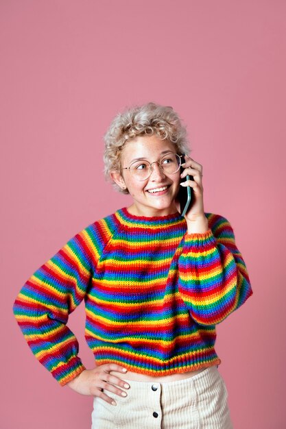 Linda chica alegre con un suéter de arco iris y una boina verde hablando por teléfono