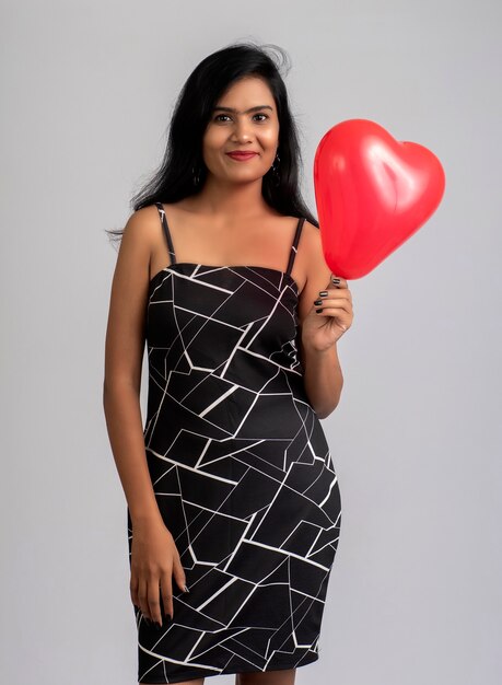 Linda chica alegre en traje elegante posando con globo en forma de corazón