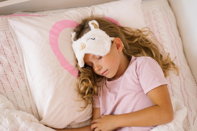 Linda chica con un antifaz para dormir duerme dulcemente sobre una almohada