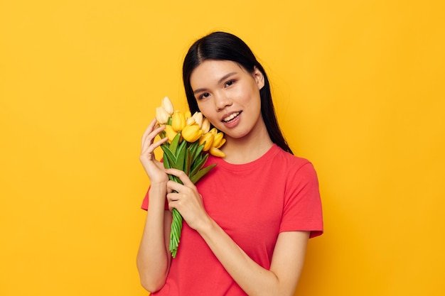 Linda chica asiática alegre con un ramo de flores de fondo amarillo