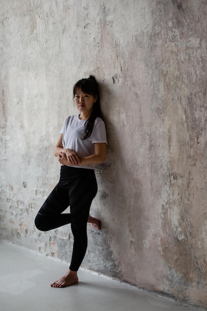 Linda chica asiática con cabello largo oscuro está de pie en la pared de elaboración en ropa de entrenamiento relajarse