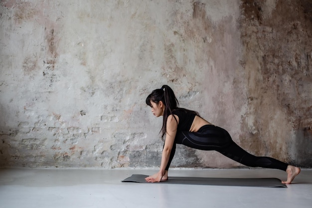 linda chica asiática con cabello largo oscuro en mallas de ropa deportiva de entrenamiento y top haciendo yoga