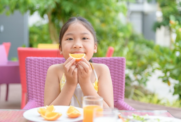 Linda chica asiática disfruta de comer naranja fresca en la mañana,