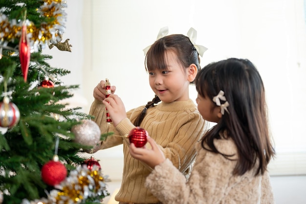 Una linda chica asiática disfruta decorando un árbol de Navidad con su hermana menor en la sala de estar