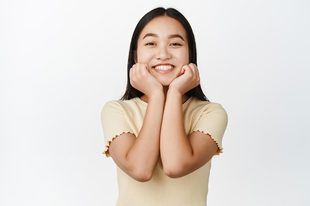 Linda chica asiática con una sonrisa blanca y saludable que se ve feliz tomados de la mano en el fondo blanco de la cara