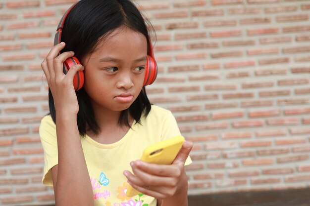 Una linda chica asiática usa un auricular inalámbrico rojo para escuchar música en su teléfono