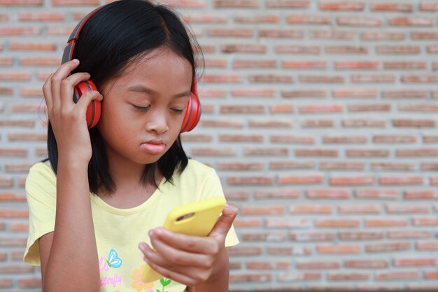 Una linda chica asiática usa un auricular inalámbrico rojo para escuchar música en su teléfono