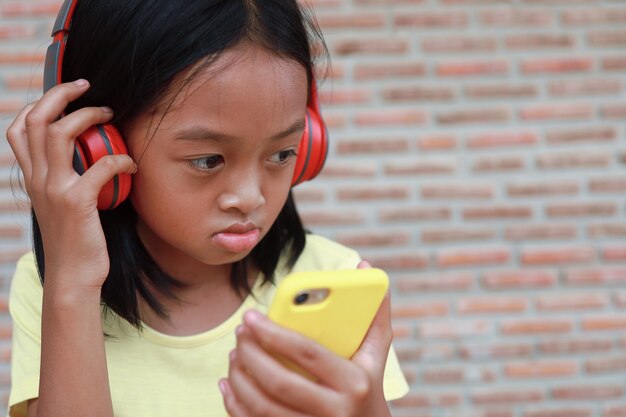 Una linda chica asiática usa un auricular inalámbrico rojo para escuchar música en su teléfono