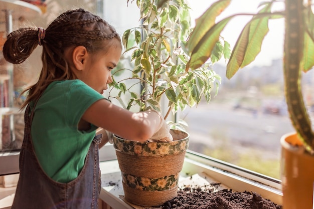 Linda chica ayudando a cuidar las plantas caseras en la ventana del balcón