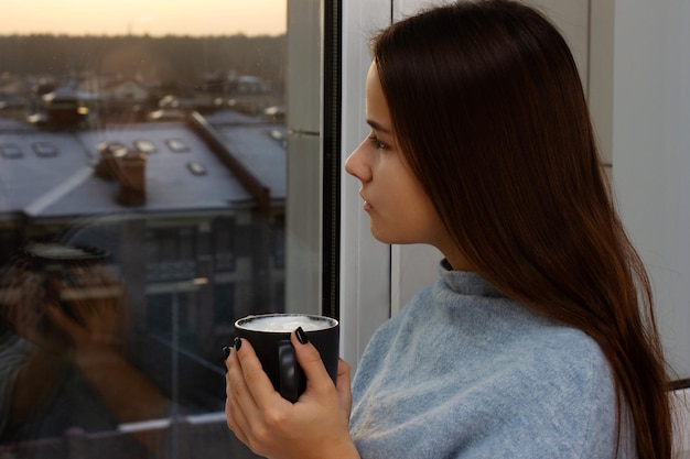 Linda chica bebe café y mira por la ventana al atardecer