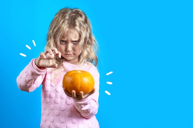 Linda chica bruja con cabello rubio evoca sobre una calabaza en azul