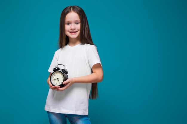 Linda chica en camiseta con pelo largo espera el reloj