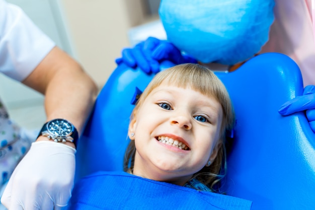 Linda chica en clínica dental. Niño en armario estomatológico con boca abierta.