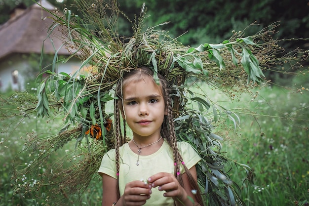Linda chica con corona de flores de verano y trigo dorado en el patio de la casa de campo