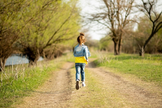 Una linda chica corre por un camino rural vacío Primavera Libertad Infancia Familia