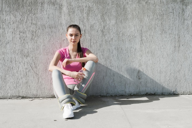 Linda chica delgada sentada en el suelo bajo el sol, ganando fuerza antes de entrenar