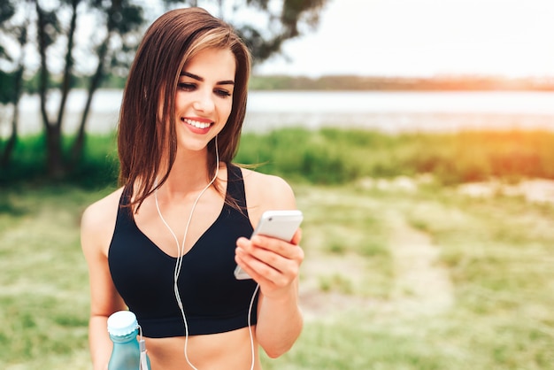 Linda chica deportiva relajante al aire libre después de entrenar con una botella de agua