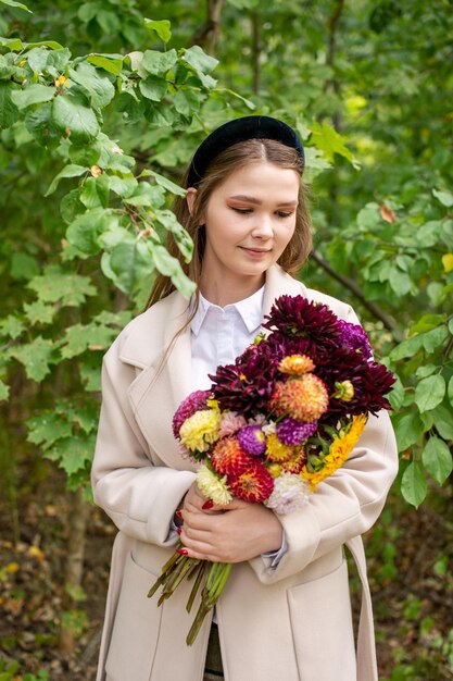 Una linda chica con una diadema negra y cabello largo sostiene un ramo de flores de otoño