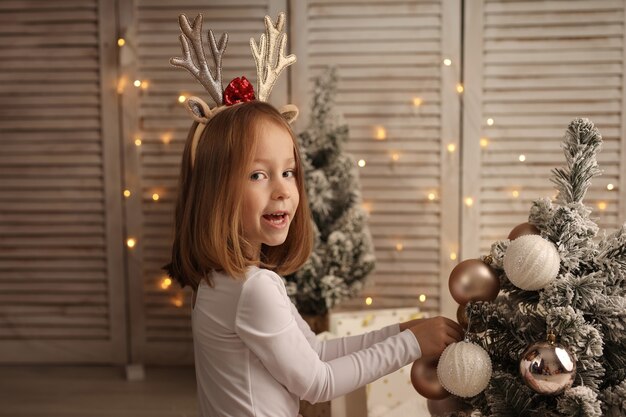 una linda chica con un disfraz de Año Nuevo decora el árbol de Navidad con globos