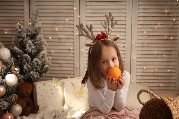 una linda chica con un disfraz de Año Nuevo sostiene una naranja en sus manos