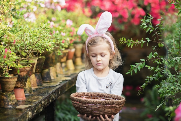 Linda chica divertida con orejas de conejo de Pascua en el jardín. concepto de pascua Niño riendo en búsqueda de huevos de Pascua