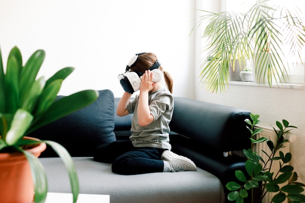 Linda chica divertida viendo algo que se muestra en gafas de realidad virtual, sentado en el sofá. Concepto de tecnología moderna