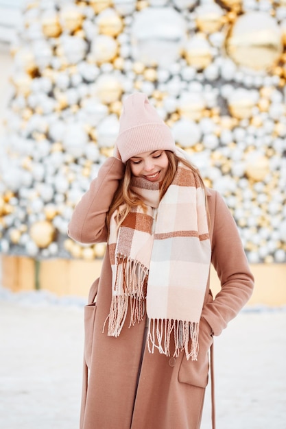 Linda chica en elegante traje de invierno posando frente a decoraciones navideñas en invierno al aire libre.