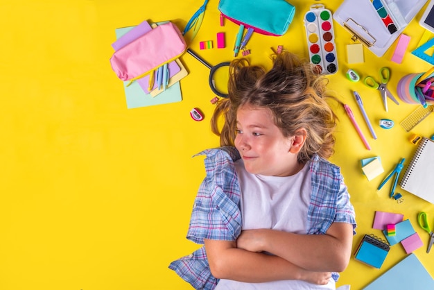 Linda chica emocional lista para volver a la escuela con varios útiles escolares accesorios educativos sobre fondo amarillo brillante