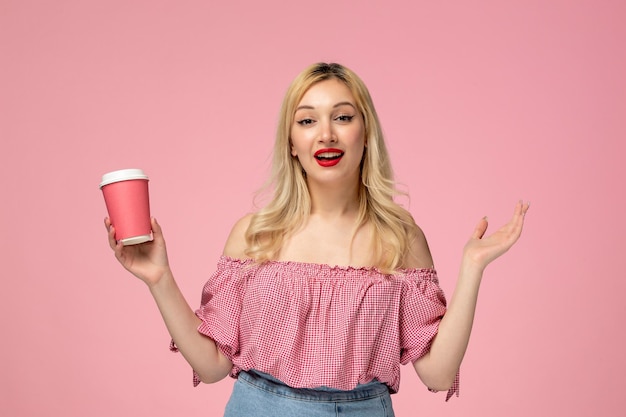 Linda chica encantadora jovencita con lápiz labial rojo en blusa rosa agitando las manos y sosteniendo una taza rosa