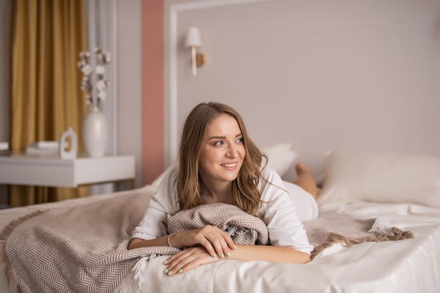 Linda chica está acostada en la cama en el dormitorio y mirando hacia otro lado