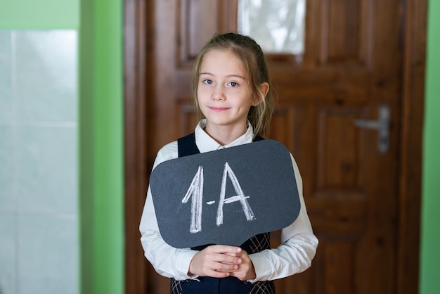 Una linda chica está de pie en el aula con un cartel de grado 1 Vida escolar