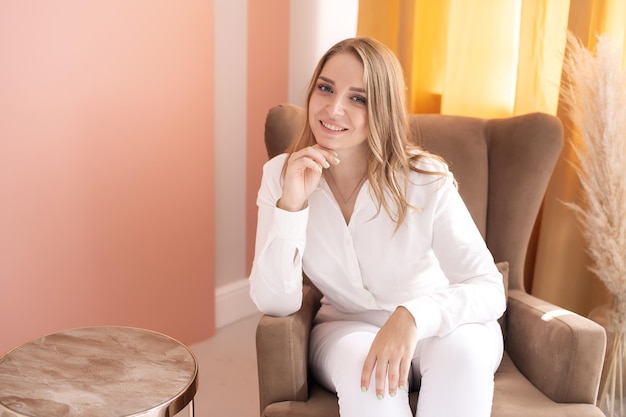 Una linda chica está sentada en una silla con la mano debajo de la cara Una habitación con paredes rosadas