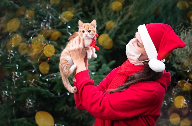 linda chica europea con un sombrero rojo de Santa recibe un pequeño gatito rojo como regalo y es feliz