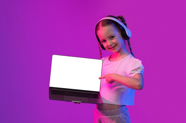 Linda chica feliz usando auriculares inalámbricos mostrando su maqueta de computadora