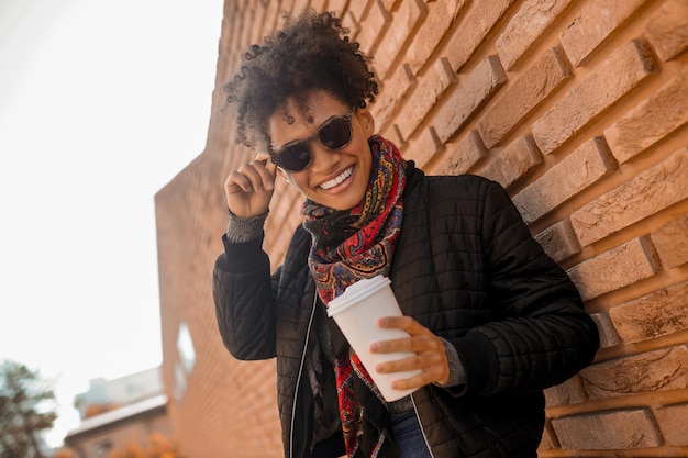 Una linda chica con gafas de sol tomando café afuera