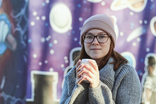 Linda chica con gafas con una taza de café en el parque