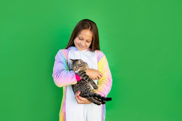 Linda chica con un gato en sus manos. Fondo verde aislado. Espacio para texto. animal como regalo.