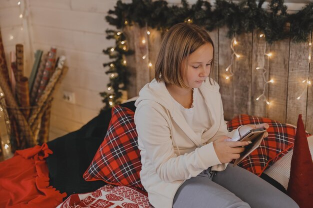 Linda chica habla en un teléfono inteligente en un ambiente navideño