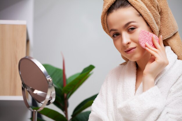 Linda chica hace maquillaje en la cara en el baño