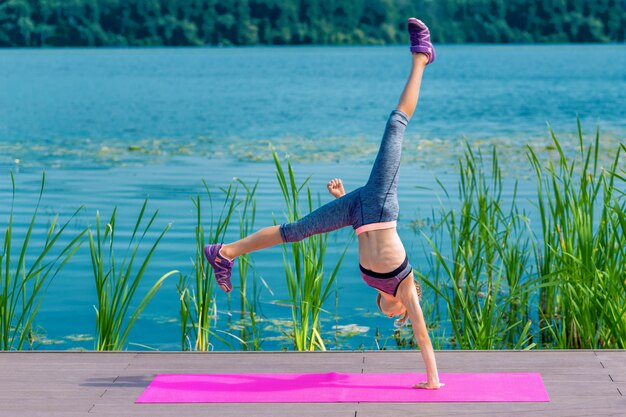 Linda chica haciendo parada de manos acrobática junto al lago