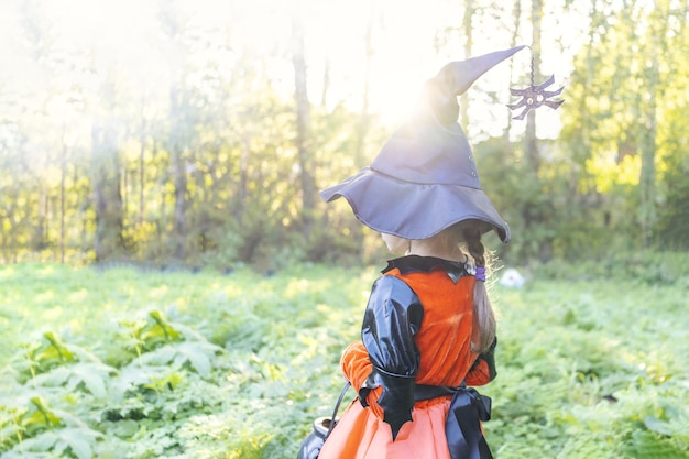 Linda chica de Halloween que va a recoger dulces. Pedir dulce o truco. Guising. Jack o lantern. Celebra halloween. en el bosque con canasta de dulces Niño en el exterior de bruja de traje de carnaval. Copie el espacio.