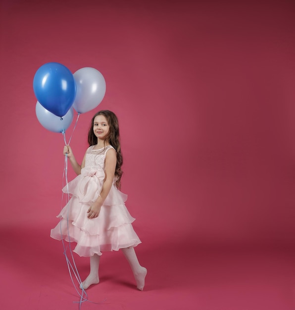 Linda chica en un hermoso vestido sosteniendo globos azules sobre un fondo brillante