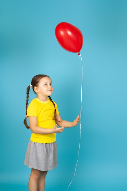 linda chica interesada en camiseta amarilla sostiene un globo rojo en forma de corazón junto a una cuerda