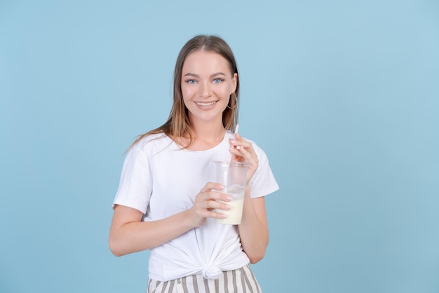 Linda chica joven caucásica en camiseta blanca y pantalones a rayas bebe batido