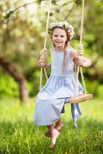 Linda chica joven divirtiéndose en un columpio en el floreciente jardín de manzano antiguo. Día soleado. Actividades al aire libre de primavera para niños