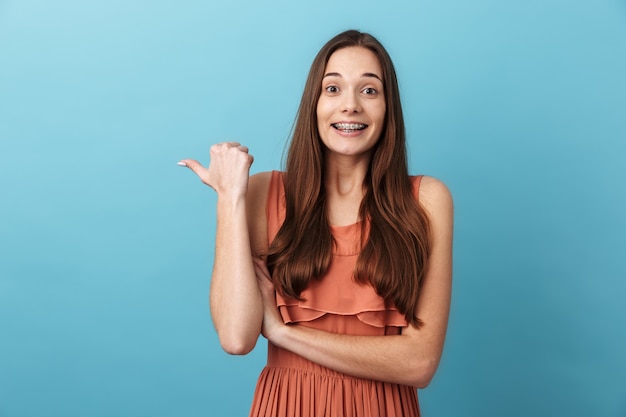 Linda chica joven encantadora alegre que se encuentran aisladas sobre la pared azul, señalando con el dedo en el espacio de copia