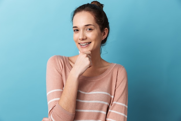 Linda chica joven encantadora que se encuentran aisladas sobre la pared azul, posando